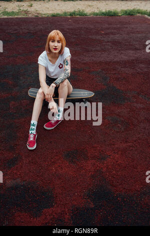 Portrait de jeune femme assise sur cool carver skateboard en plein air Banque D'Images