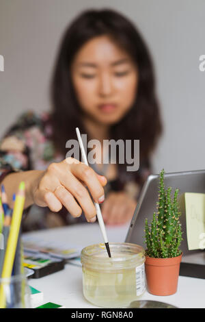 Illustrator en peinture à un bureau dans un atelier, close-up Banque D'Images