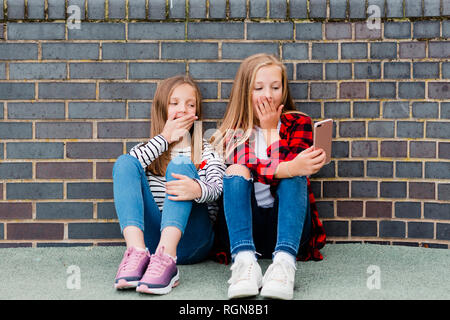 Portrait de deux jeunes filles assis devant un mur de briques en tenant avec smartphone selfies Banque D'Images