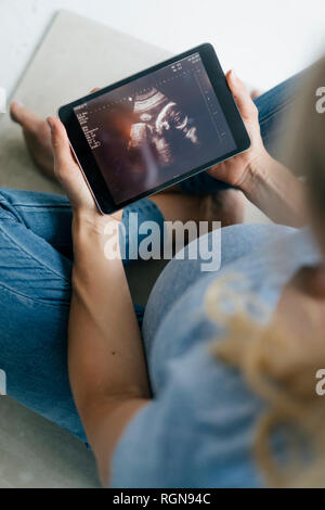 Femme enceinte, assise sur le sol à l'échographie à photo sur tablette Banque D'Images