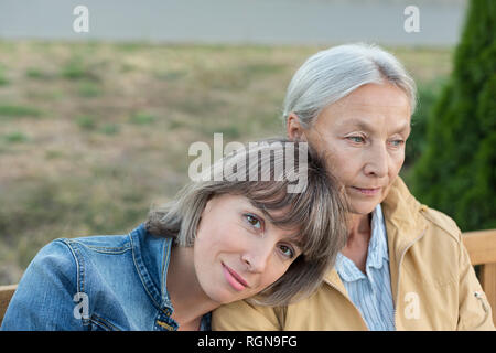 Portrait of young woman sitting on bench avec sa mère à l'extérieur Banque D'Images