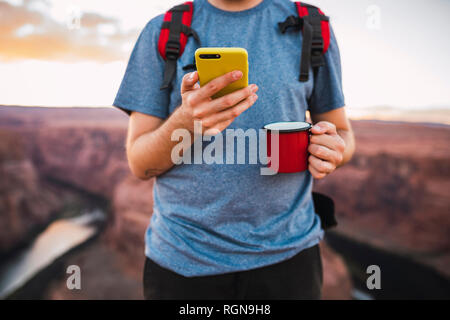 Young man holding red cup et using smartphone Banque D'Images