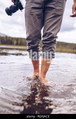 La Suède, la Laponie, l'homme avec l'appareil photo de patauger dans l'eau, vue partielle Banque D'Images