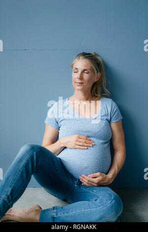 Portrait of smiling pregnant woman sitting on the floor with closed eyes Banque D'Images