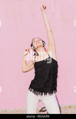 Happy young woman wearing headphones danser devant un mur rose Banque D'Images