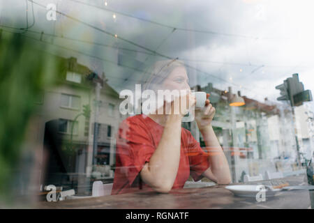 Jeune femme avec tasse de café derrière la vitre dans un café Banque D'Images