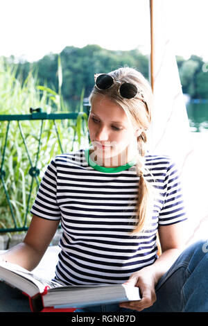 Young woman reading book à un lac à côté de bateau à voile Banque D'Images