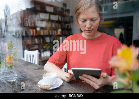 Jeune femme à l'aide de comprimé à la fenêtre dans un café