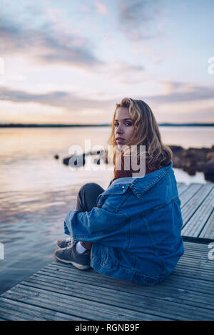 Jeune femme assise au bord du lac Inari, looking at camera, Finlande Banque D'Images