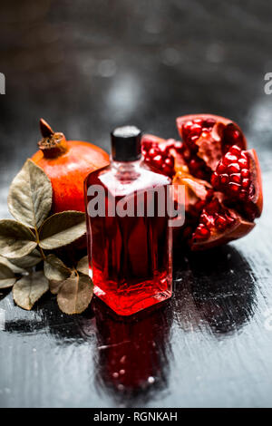 Close up d'huile essentielle de la Grenade Grenade mûre avec des matières sur la surface en bois en bouteille transparente. Banque D'Images