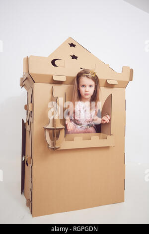 Petite Princesse en couronne joue avec son château en carton. Une émotion vraie du bonheur de l'enfant. Banque D'Images