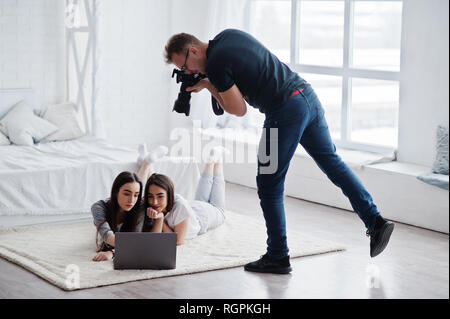 Prise de vue photographe studio sur deux modèles jumeaux qui sont à la recherche à l'ordinateur portable. Photographe professionnel sur le travail. Classe de maître. Banque D'Images