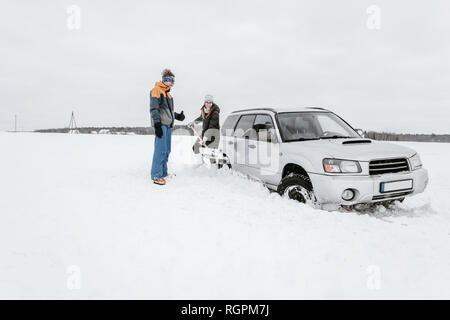 Jeune femme avec pelle creuser la neige d'automobile près de guy en hiver l'usure de prairie à Vilnius, Lituanie Banque D'Images