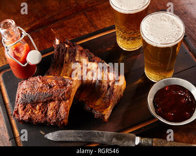 Deux portions de côtes levées grillées épicées servi avec de la bière fraîche et un couteau sur un plateau dans une taverne ou au pub Banque D'Images