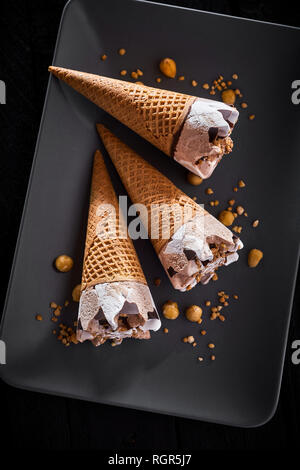 Glaces surgelées dans sugar cones servi sur une plaque noire rectangulaire moderne avec quelques noix, hachées Banque D'Images