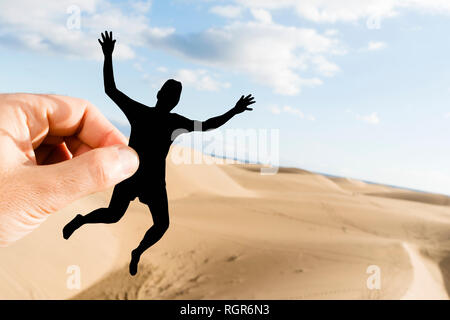 Libre de la main d'un homme de race blanche tenant une découpe du papier sous la forme d'un jeune homme s'amusant sur les dunes de sable Banque D'Images