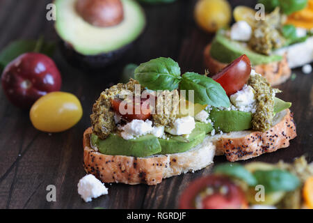 Toast à l'avocat sandwich avec les avocats, le pesto, le fromage feta, basilic frais du jardin et heirloom tomatoes, sur un fond de bois rustique. Fo grec Banque D'Images