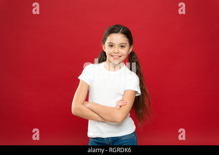 Elle est vraiment mignonne. Fashion look de petit modèle. Peu de fashionista. Fashion girl sur fond rouge. Adorable petite fille dans un style décontracté. Petit enfant avec des cheveux longs. Heureux petit enfant. Banque D'Images