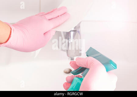 Une femme se lave les gants rose avec un lavabo blanc et d'un robinet de la salle de bain à la maison avec des serviettes et de pulvérisation. Le travail de routine Banque D'Images