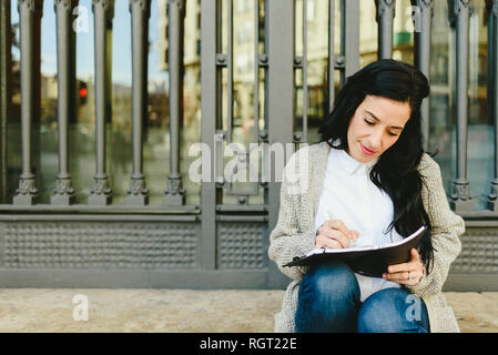 Portrait of young woman en prenant des notes dans son carnet, la lecture de plans, vue de face. Banque D'Images