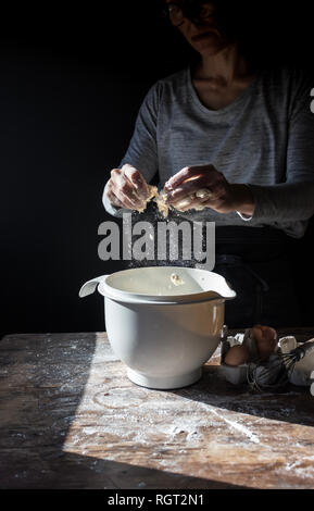 Les droits de récolte des oeufs casser dans un bol sur la table en bois avec de la farine sur fond noir Banque D'Images