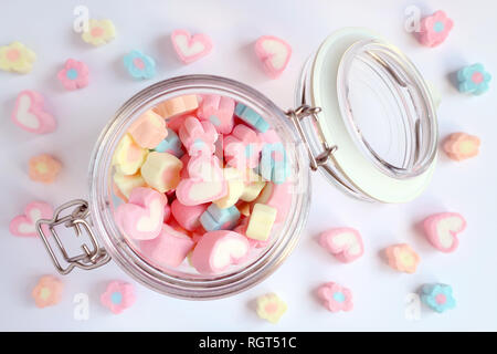 Vue de dessus de couleur pastel et coeur en forme de fleurs bonbons guimauve dans un bocal en verre avec un peu éparpillés sur la table bleu pâle, Valentine concept Banque D'Images