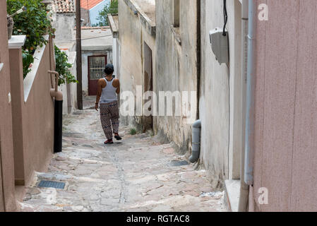 Femme descendant des escaliers sur la rue de village grec avec chapeau et tank top Banque D'Images