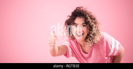 Portrait de jeune fille gaie belle avec des cheveux bouclés et lâche t-shirt rose isolé sur fond rose, pour femme, Texte et concept emotio Banque D'Images