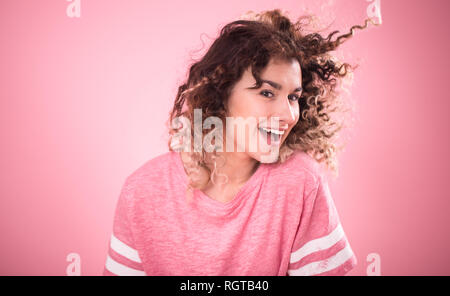 Portrait de jeune fille gaie belle avec des cheveux bouclés et lâche t-shirt rose isolé sur fond rose, pour femme, Texte et concept emotio Banque D'Images