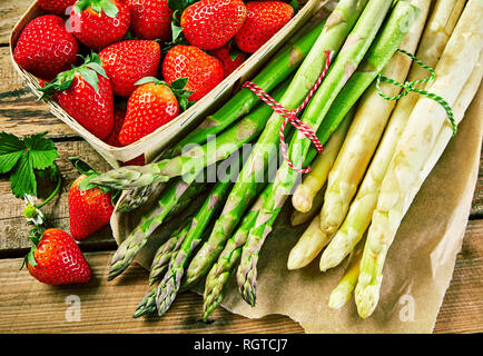 Des paquets de blanc et vert frais asperges du printemps avec un rouge mûr de Punnett Fraises Juteuses sur une table en bois dans une vue en gros plan Banque D'Images