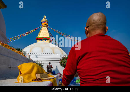 Le grand stupa avec des drapeaux de prière flottant dans la banlieue Boudha assis, un moine bouddhiste et priant ci-dessous Banque D'Images