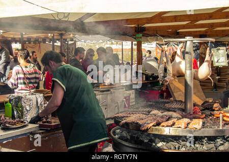 Cordoue, Espagne - 26 janvier 2018 : chef cooking in restaurant en plein air plein de gros morceaux de viande et les cochons ensemble. Les touristes profiter de la journée. Banque D'Images