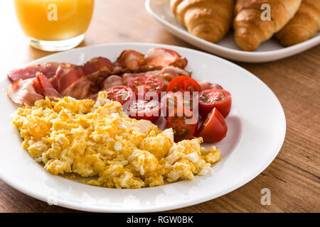 Petit-déjeuner avec des œufs brouillés, bacon, tomates, jus d'orange et un croissant sur la table en bois Banque D'Images