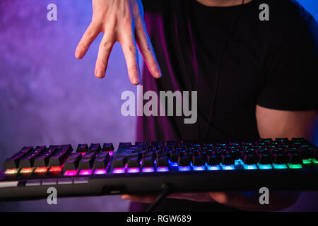 Gros plan sur les mains du joueur va presser une touche sur un clavier. Le fond est éclairé avec des néons Banque D'Images