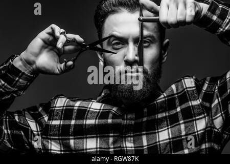 Jeune homme séduisant coiffure ou de coiffure avec barbe, habillé en chemise à carreaux démontrant une lame tranchante de son bord droit rasoir de barbier et de la SCIS Banque D'Images