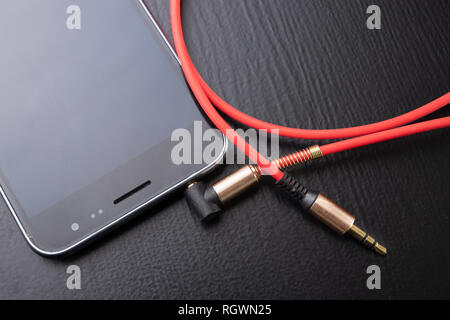 Jack câble pour brancher le casque. Téléphone et les accessoires sur la table. Fond sombre. Banque D'Images