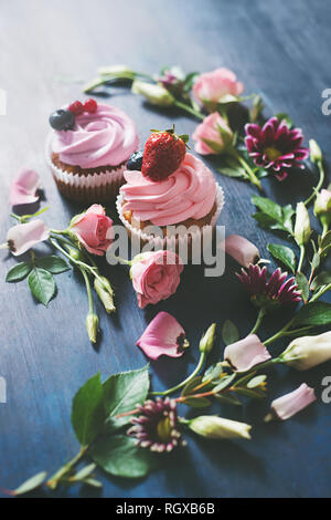 Cupcakes avec fraises et fleurs rose sur un fond sombre. Dessert de printemps concept avec copie espace Banque D'Images