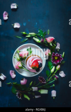 Cupcakes avec fraises et fleurs rose sur un fond sombre. Dessert de printemps concept avec copie espace Banque D'Images