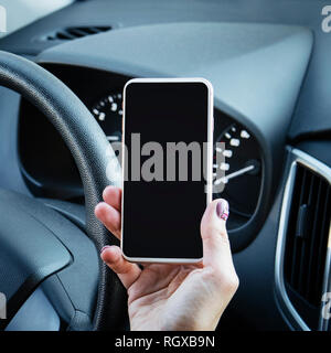 Close up of woman's hand holding mobile phone avec écran noir au volant d'une voiture. Femme à l'aide de smart phone assis dans le siège du conducteur. Girl arrête la c Banque D'Images