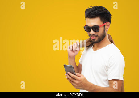L'homme d'affaires asiatique bel homme avec une moustache, sourire et rire et à l'aide de smart phone sur fond jaune Banque D'Images