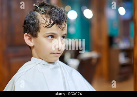 Portrait en gros plan d'un mignon petit garçon assis sur une chaise avec une berline blanche cape et en attente d'une coiffure Banque D'Images