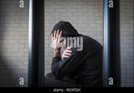 Un prisonnier avec sa tête dans ses mains derrière les barreaux dans une cellule de prison (photo posée par modèle) Banque D'Images