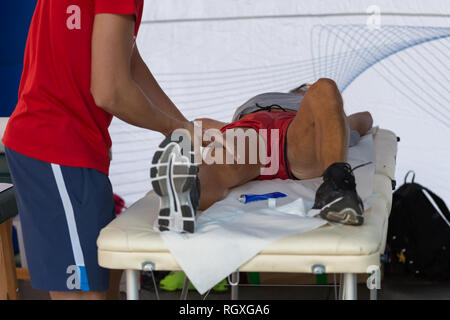 Étendu sur un lit de l'athlète tout en ayant les jambes massées après un entraînement physiques sportives. Banque D'Images