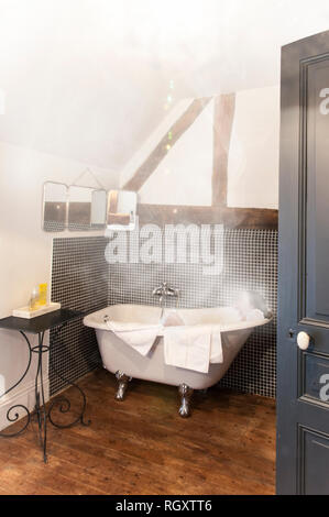 Woman relaxing in old fashioned retro steamy une baignoire sur pieds. Plancher de bois, support en fer forgé, miroir mural, carreaux, et ouvrez la porte. Banque D'Images