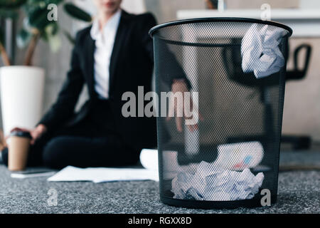 Focus sélectif de papier froissé dans panier alors que businesswoman sitting on floor Banque D'Images