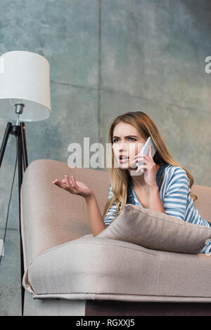 Worried Woman talking on smartphone et couché sur un canapé rose Banque D'Images