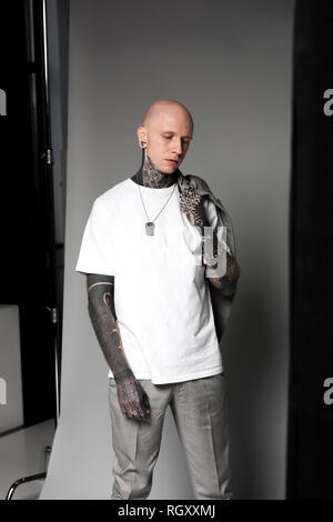 Jeune homme chauve avec des tatouages holding veston sur l'épaule et en studio permanent Banque D'Images