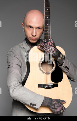 Handsome bald tattooed man hugging guitare acoustique isolé sur gray Banque D'Images