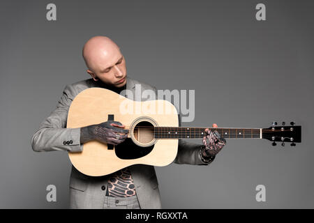 Handsome bald tattooed man playing acoustic guitar isolé sur gray Banque D'Images