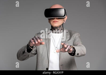 Tattooed man élégant à l'aide de casque de réalité virtuelle isolé sur gray Banque D'Images